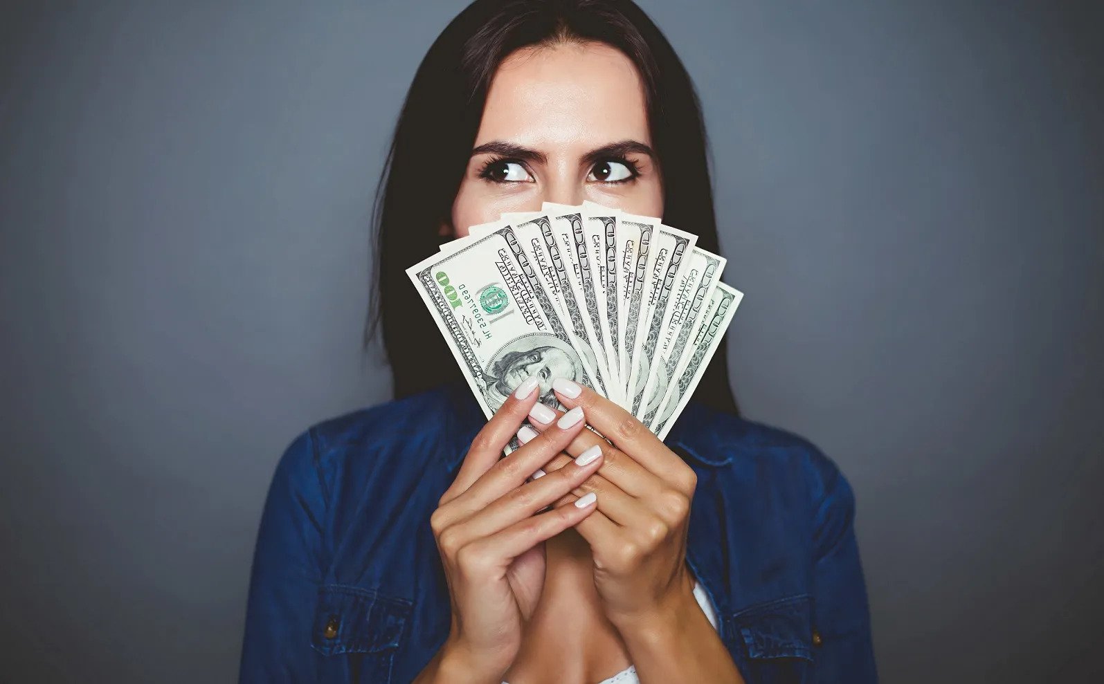 woman holding dollar bills like a fan in front of her face